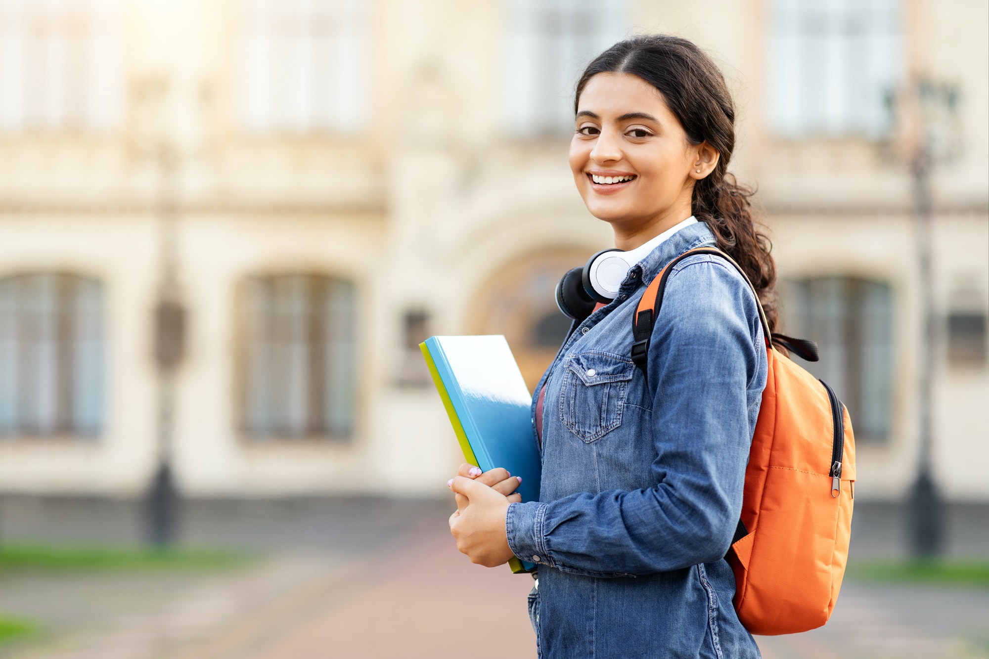 Contented young Indian academic lady with course materials and backpack