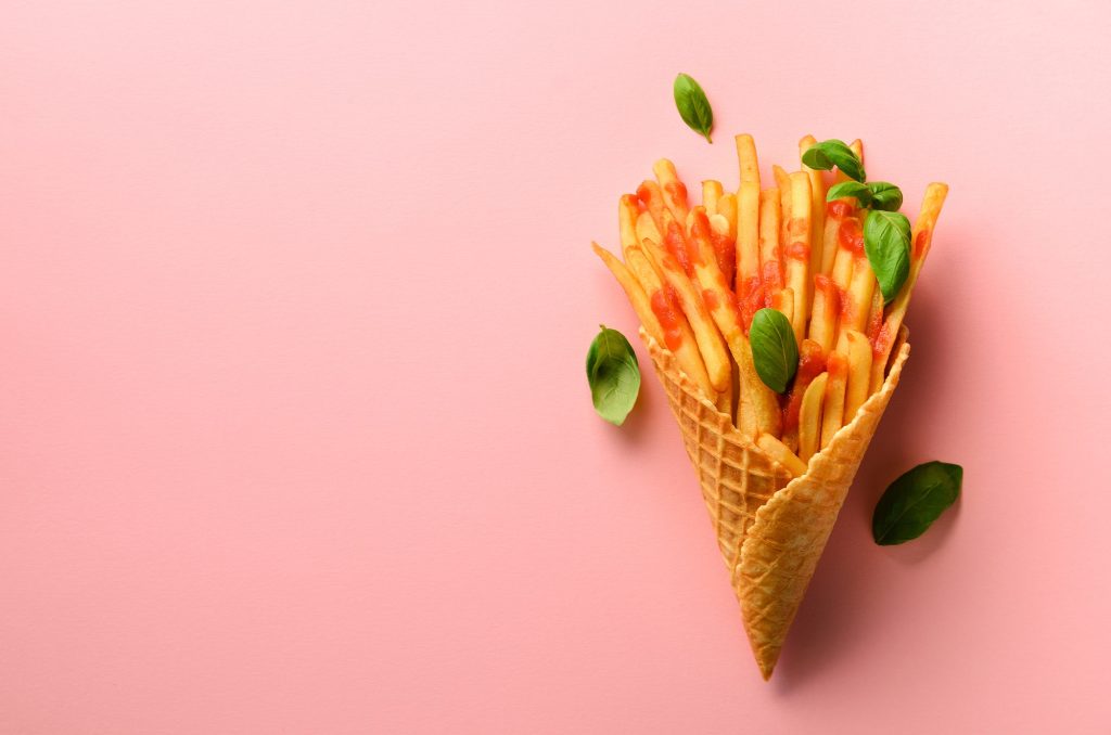 Fried potatoes in waffle cones on pink background. Hot salty french fries with sauce, basil leaves
