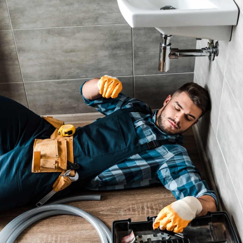 bearded-handyman-lying-on-floor-near-toolbox-in-bathroom.jpg